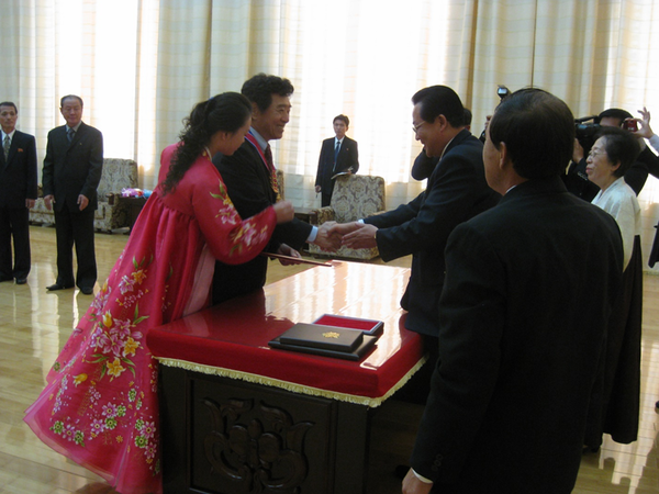 ▲ 2012년 10월 만수대 의사당에서, 국가학위학직수여위원회장 김용진 부총리(교육상)로부터 명예의학박사학증을 받았다. 김 부총리나 나나 근엄하지 않고 서로 웃는 모습이다.